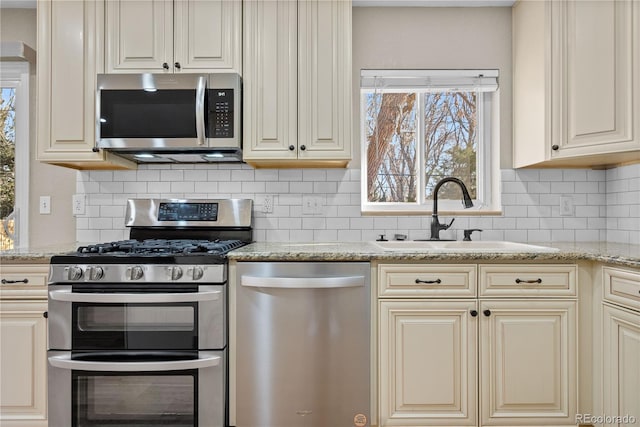 kitchen with decorative backsplash, cream cabinetry, appliances with stainless steel finishes, and a sink