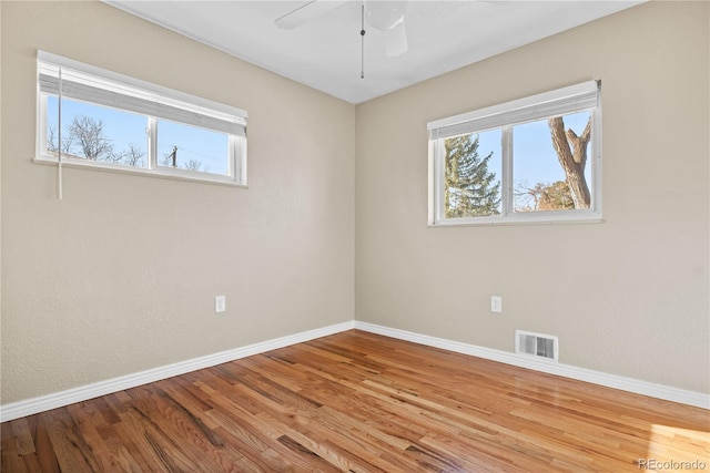 empty room with visible vents, a healthy amount of sunlight, baseboards, and wood finished floors