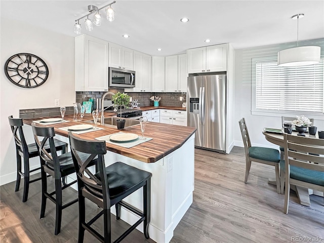 kitchen with a peninsula, butcher block countertops, appliances with stainless steel finishes, white cabinetry, and tasteful backsplash