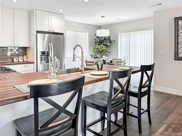 kitchen featuring decorative light fixtures, backsplash, white cabinets, stainless steel fridge with ice dispenser, and butcher block countertops