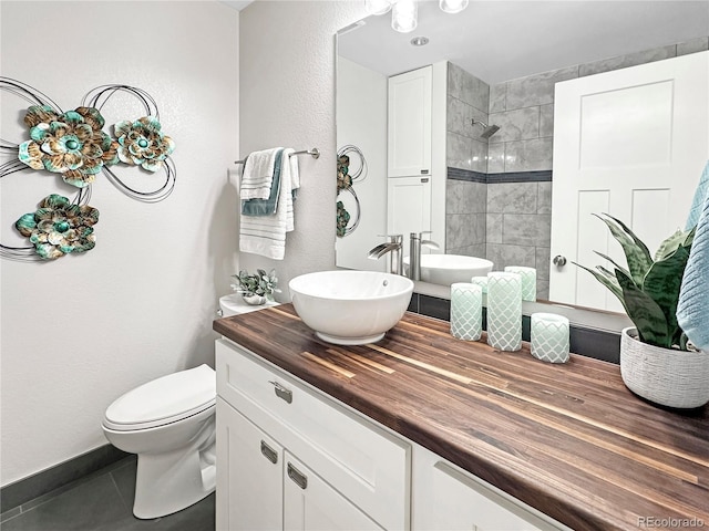 full bath with vanity, a tile shower, tile patterned floors, toilet, and a textured wall