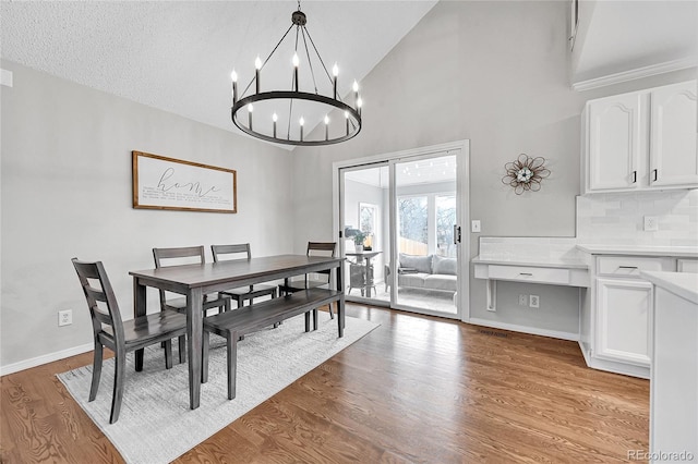 dining area featuring an inviting chandelier, high vaulted ceiling, a textured ceiling, and light wood-type flooring