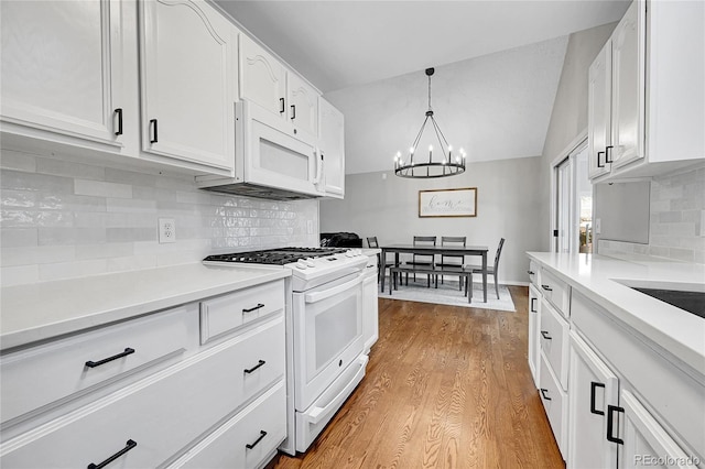 kitchen featuring white appliances, lofted ceiling, white cabinets, hanging light fixtures, and a notable chandelier