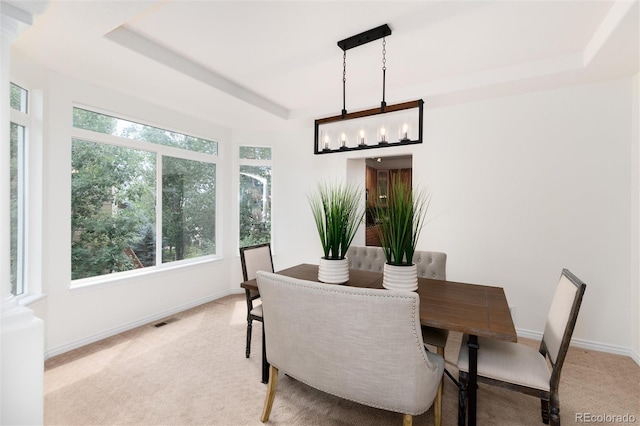 carpeted dining area with a raised ceiling, plenty of natural light, and an inviting chandelier