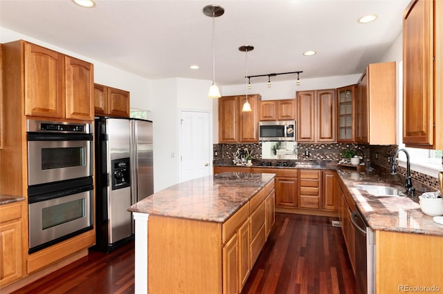 kitchen featuring sink, a center island, dark stone countertops, pendant lighting, and appliances with stainless steel finishes