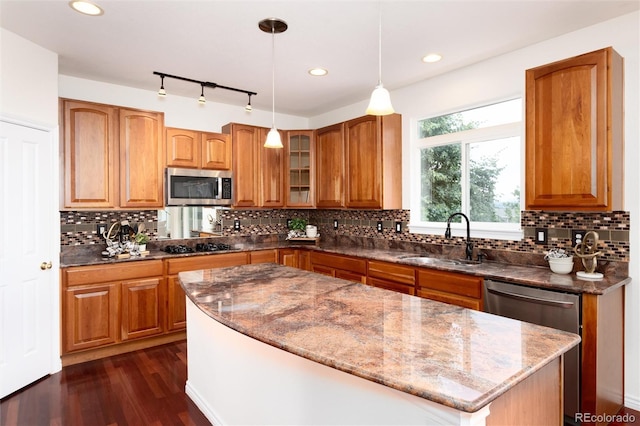 kitchen featuring appliances with stainless steel finishes, dark hardwood / wood-style flooring, dark stone counters, sink, and hanging light fixtures