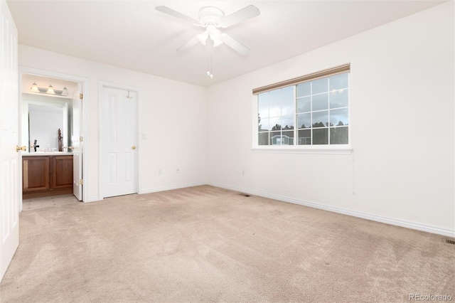 unfurnished bedroom featuring light colored carpet, ensuite bath, and ceiling fan