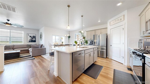 13488 Wabash St, Thornton, CO 80602 - kitchen featuring appliances with stainless steel finishes, a sink, open floor plan, ceiling fan, and light wood finished floors
