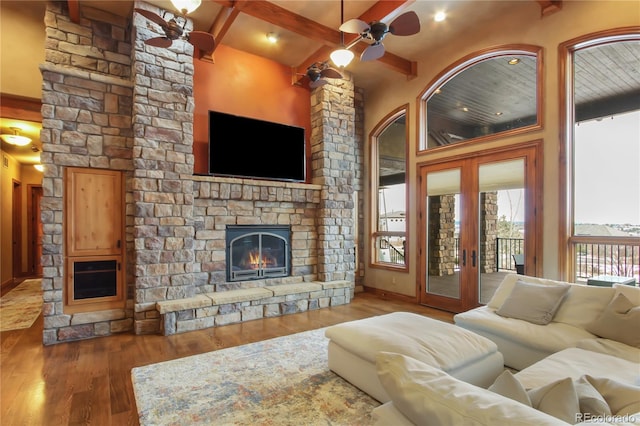 living room featuring dark wood-type flooring, french doors, a stone fireplace, beamed ceiling, and ceiling fan