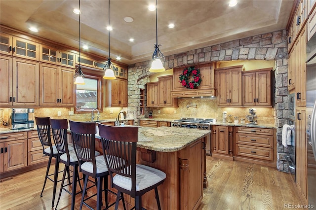 kitchen featuring a breakfast bar, light stone countertops, a center island with sink, a raised ceiling, and light wood-type flooring