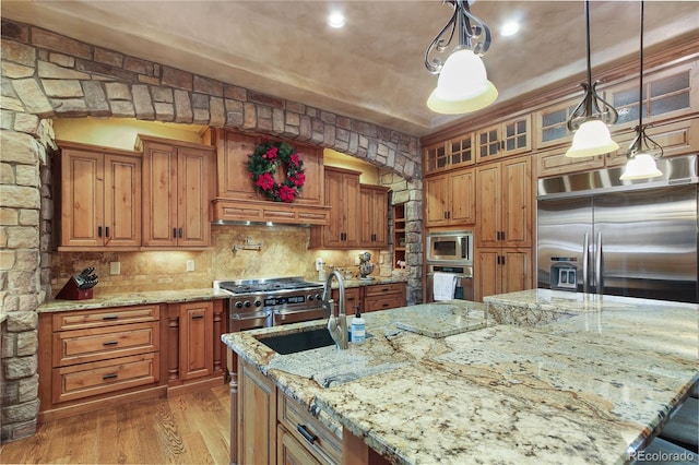 kitchen featuring wood-type flooring, sink, hanging light fixtures, built in appliances, and light stone countertops