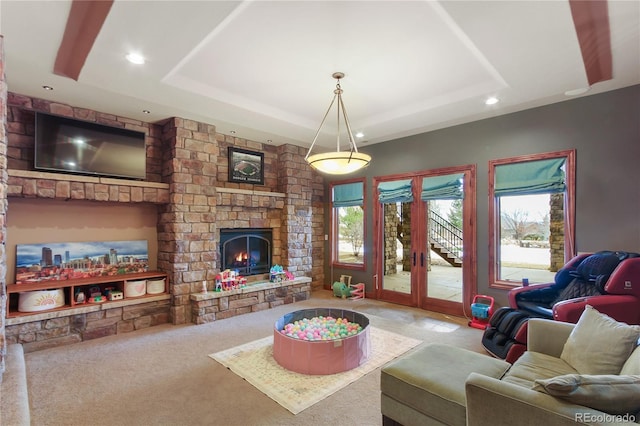 living room with a raised ceiling, a stone fireplace, carpet flooring, and french doors