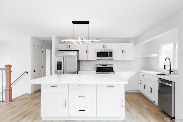 kitchen with stainless steel appliances, a sink, backsplash, light wood finished floors, and a kitchen island