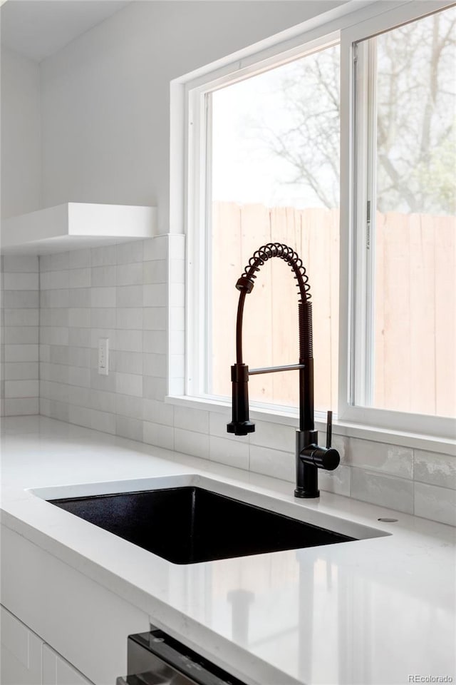 kitchen view of backsplash, a sink, and light countertops