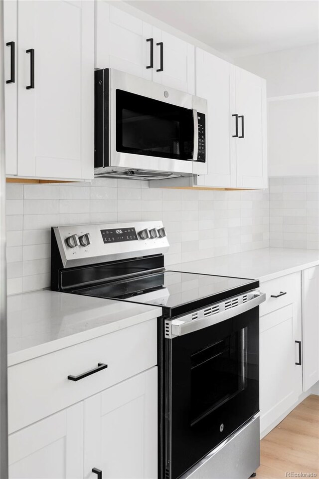 kitchen with appliances with stainless steel finishes, white cabinetry, tasteful backsplash, and light wood-style flooring