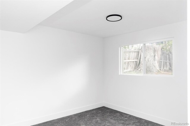 unfurnished room with baseboards and dark carpet