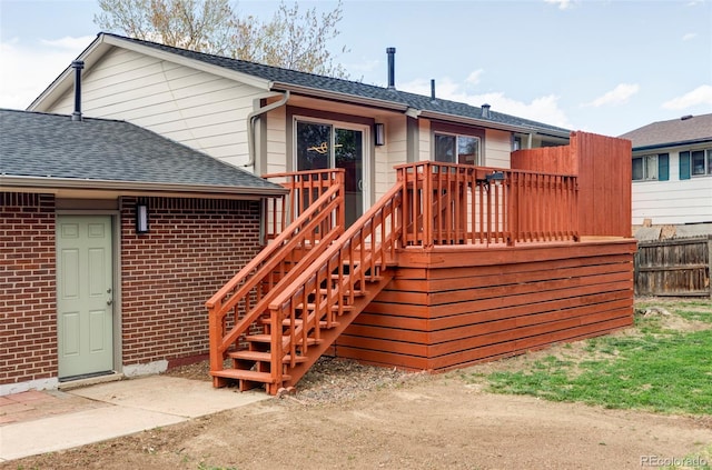 rear view of property featuring a deck, brick siding, a shingled roof, fence, and stairs
