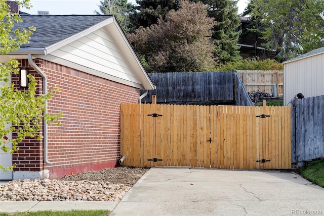 view of home's exterior with brick siding, a gate, roof with shingles, and fence