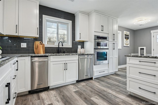 kitchen with a sink, decorative backsplash, light wood-type flooring, and appliances with stainless steel finishes