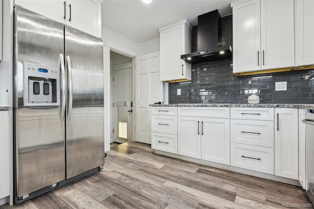 kitchen with white cabinetry, wall chimney range hood, light stone countertops, and stainless steel refrigerator with ice dispenser