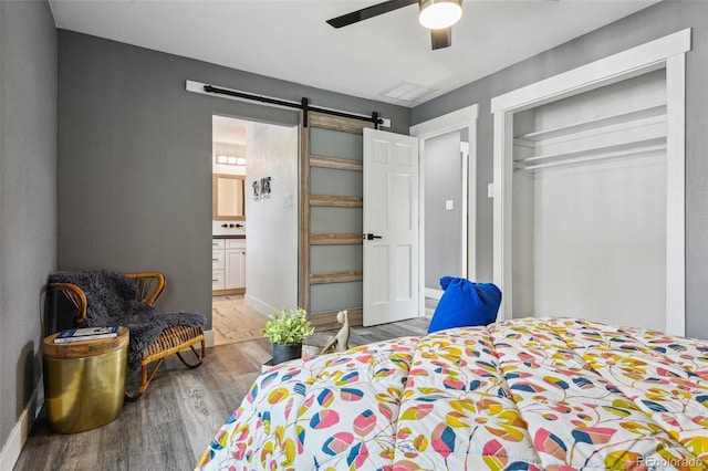 bedroom with ensuite bathroom, wood finished floors, a barn door, ceiling fan, and baseboards