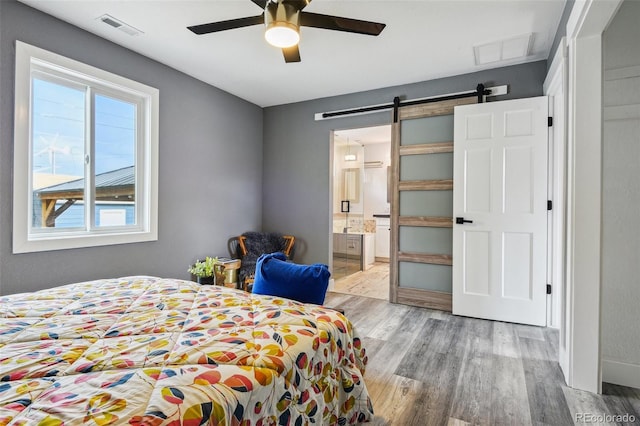 bedroom with a barn door, ensuite bath, visible vents, and wood finished floors