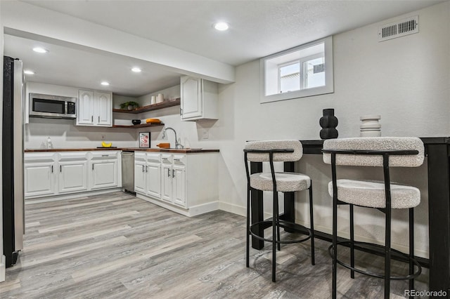 kitchen with open shelves, stainless steel appliances, white cabinetry, visible vents, and light wood-style floors