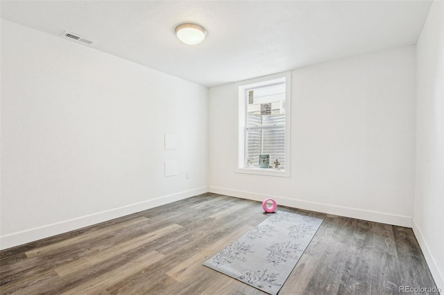 spare room with wood finished floors, visible vents, and baseboards