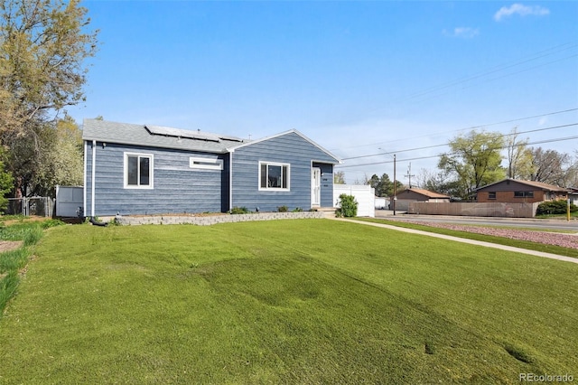 single story home with roof mounted solar panels, fence, and a front lawn