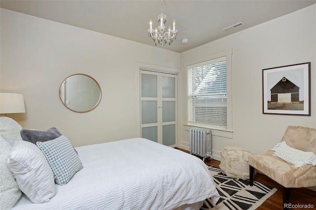 bedroom featuring an inviting chandelier, wood finished floors, visible vents, and radiator