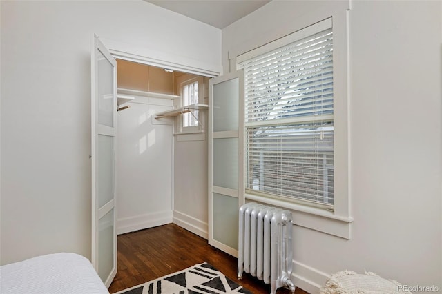 bedroom with a closet, radiator, baseboards, and wood finished floors