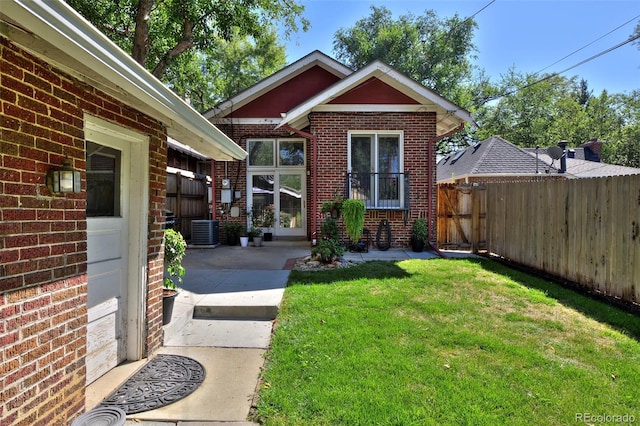 entrance to property with brick siding, a yard, a patio, central air condition unit, and fence