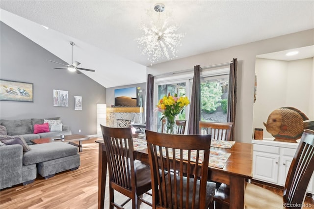 dining area with a textured ceiling, ceiling fan with notable chandelier, light wood-style flooring, and lofted ceiling