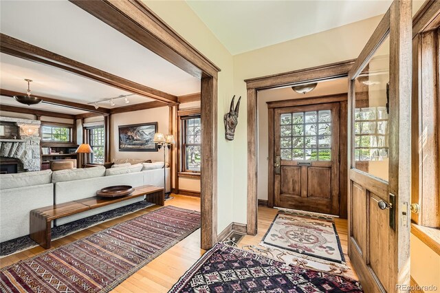 foyer featuring light wood-style flooring, a healthy amount of sunlight, and beam ceiling