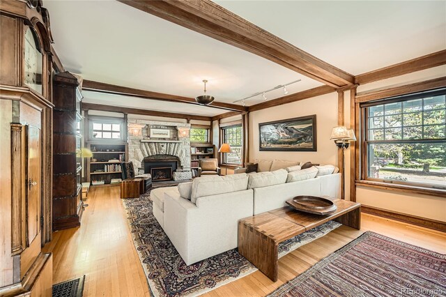 living area featuring light wood-style flooring, a fireplace, beam ceiling, and rail lighting