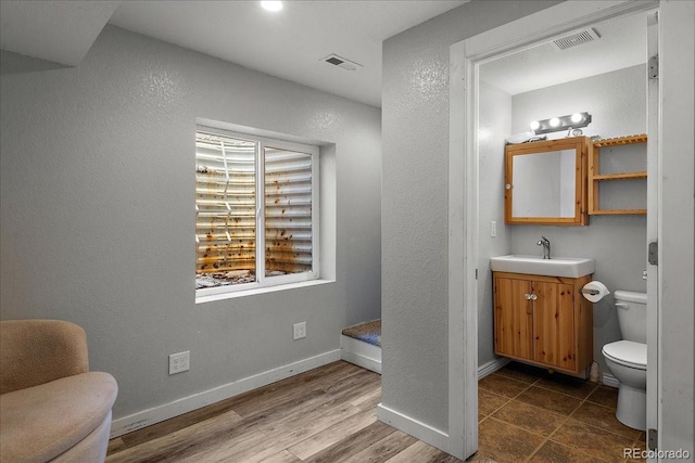 bathroom with baseboards, visible vents, toilet, and wood finished floors