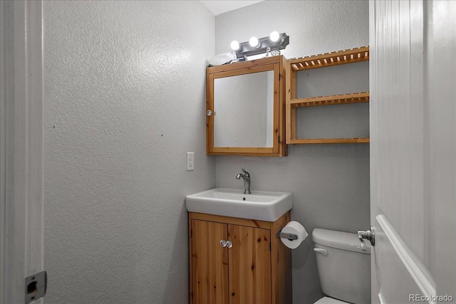 bathroom featuring a textured wall, vanity, and toilet