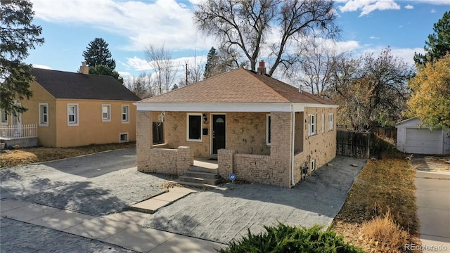 bungalow with a shingled roof, an outbuilding, covered porch, and a chimney