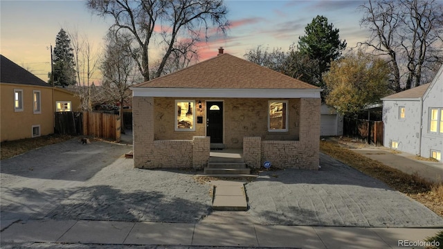 bungalow featuring covered porch, driveway, roof with shingles, and fence