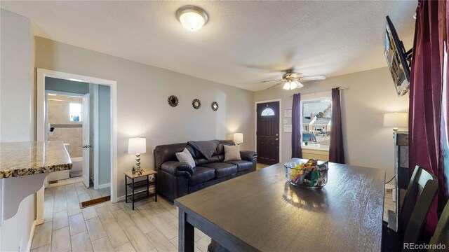 living area featuring light wood-style flooring, a textured ceiling, baseboards, and a ceiling fan