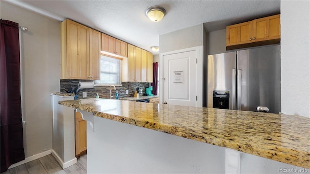 kitchen with light wood finished floors, tasteful backsplash, baseboards, light stone counters, and stainless steel refrigerator with ice dispenser