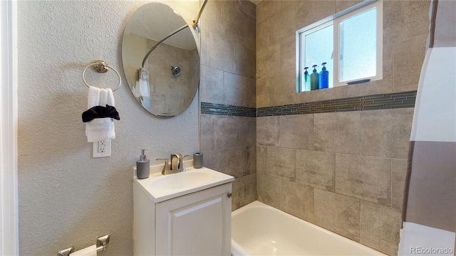 bathroom with tub / shower combination, a textured wall, and vanity