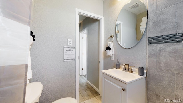 half bathroom featuring visible vents, a textured wall, vanity, and toilet