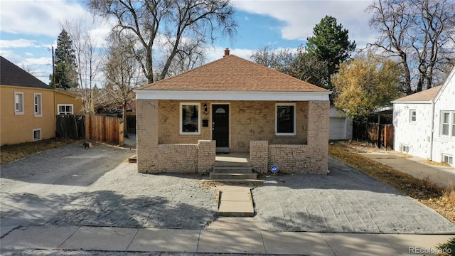 bungalow-style house featuring a shingled roof, covered porch, fence, and driveway