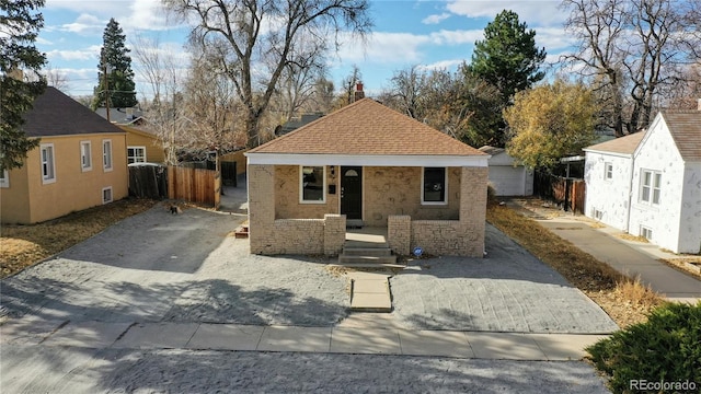 bungalow-style home featuring a porch, a shingled roof, brick siding, fence, and driveway