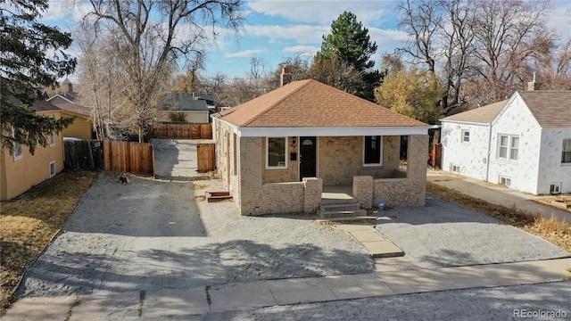 bungalow featuring driveway, roof with shingles, fence, a porch, and brick siding