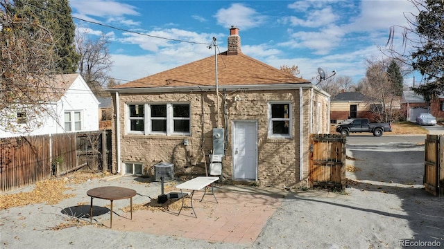 back of house with stone siding, a chimney, roof with shingles, fence, and a patio area