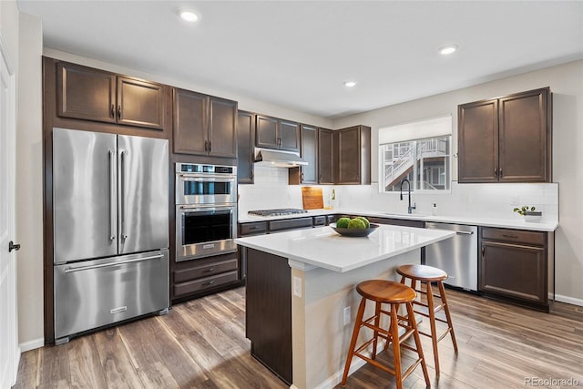 138 Lullaby Ln, Castle Rock, CO 80109 - kitchen with stainless steel appliances, a sink, under cabinet range hood, dark brown cabinets, and wood finished floors