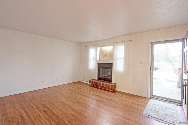 unfurnished living room featuring light wood-style flooring, baseboards, and a brick fireplace