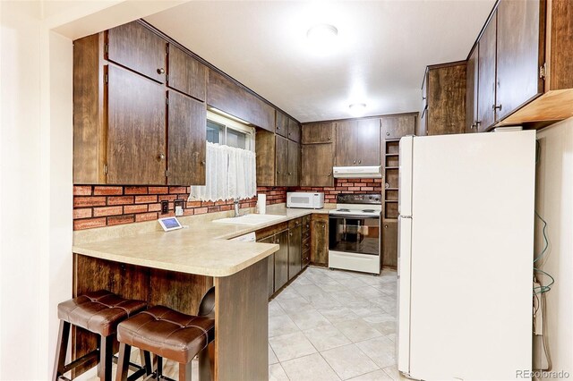 kitchen with white appliances, a sink, under cabinet range hood, a peninsula, and backsplash